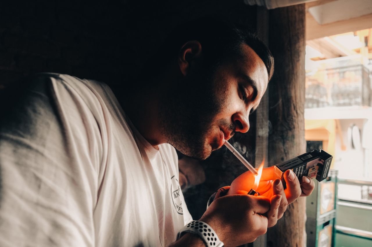 Man lights cigarette with intensity, highlighting themes of smoking and addiction indoors.