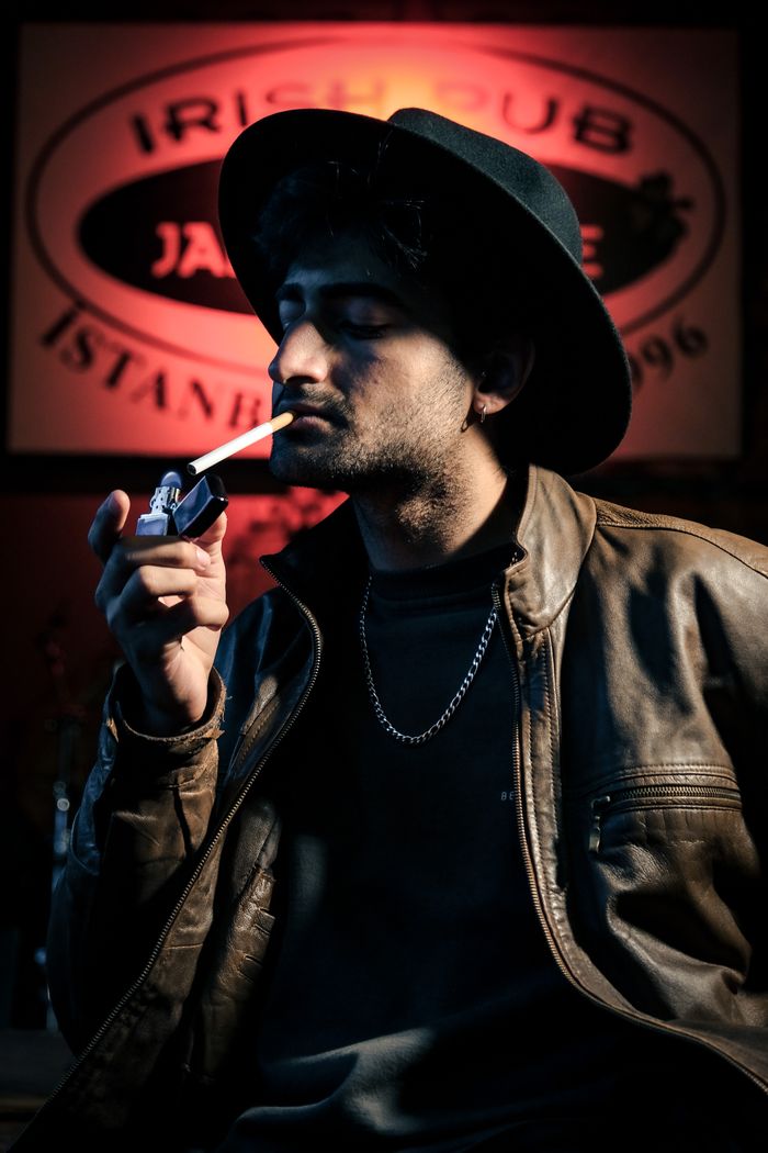 Portrait of a man smoking in a pub, wearing a hat and leather jacket, with dramatic lighting.